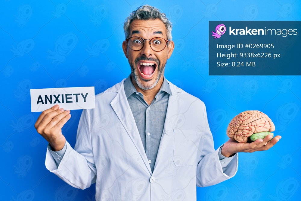Middle age grey-haired man wearing doctor coat holding brain and anxiety message celebrating crazy and amazed for success with open eyes screaming excited. 