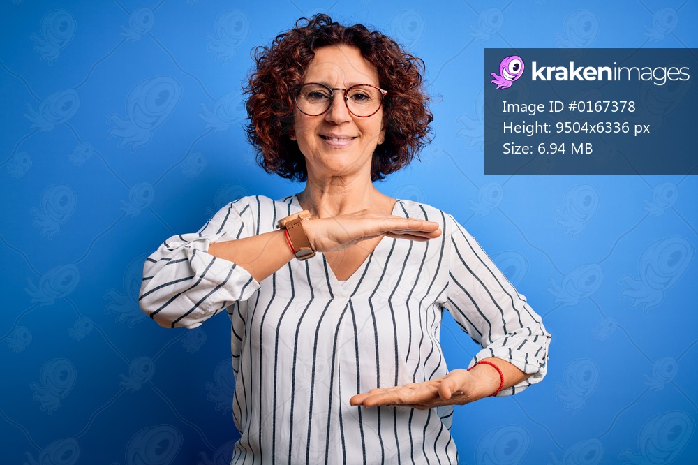 Middle age beautiful curly hair woman wearing casual striped shirt over isolated background gesturing with hands showing big and large size sign, measure symbol. Smiling looking at the camera. Measuring concept.