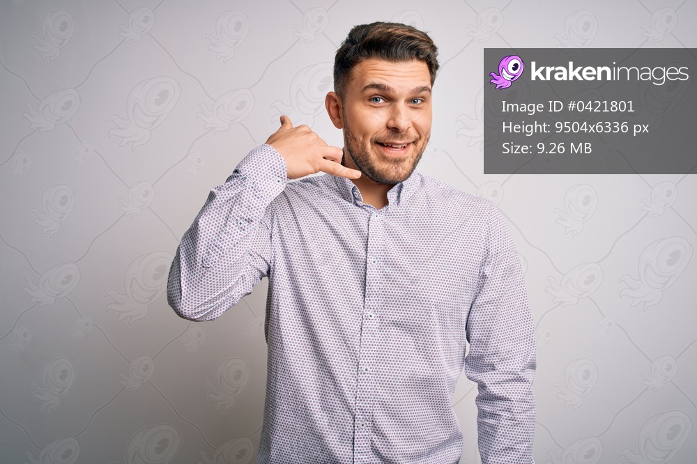 Young business man with blue eyes standing over isolated background smiling doing phone gesture with hand and fingers like talking on the telephone. Communicating concepts.