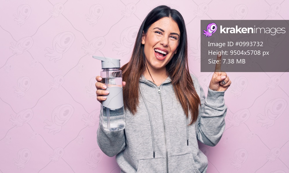 Young beautiful brunette sporty woman drinking bottle of water over isolated pink background smiling with an idea or question pointing finger with happy face, number one