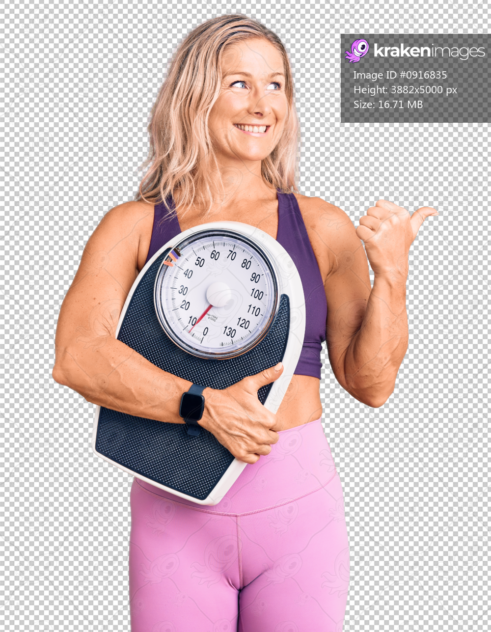 Middle age fit blonde woman wearing sports clothes holding weighing machine pointing thumb up to the side smiling happy with open mouth