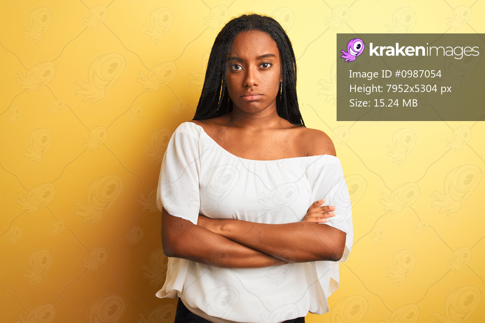 Young african american woman wearing white t-shirt standing over isolated yellow background skeptic and nervous, disapproving expression on face with crossed arms. Negative person.