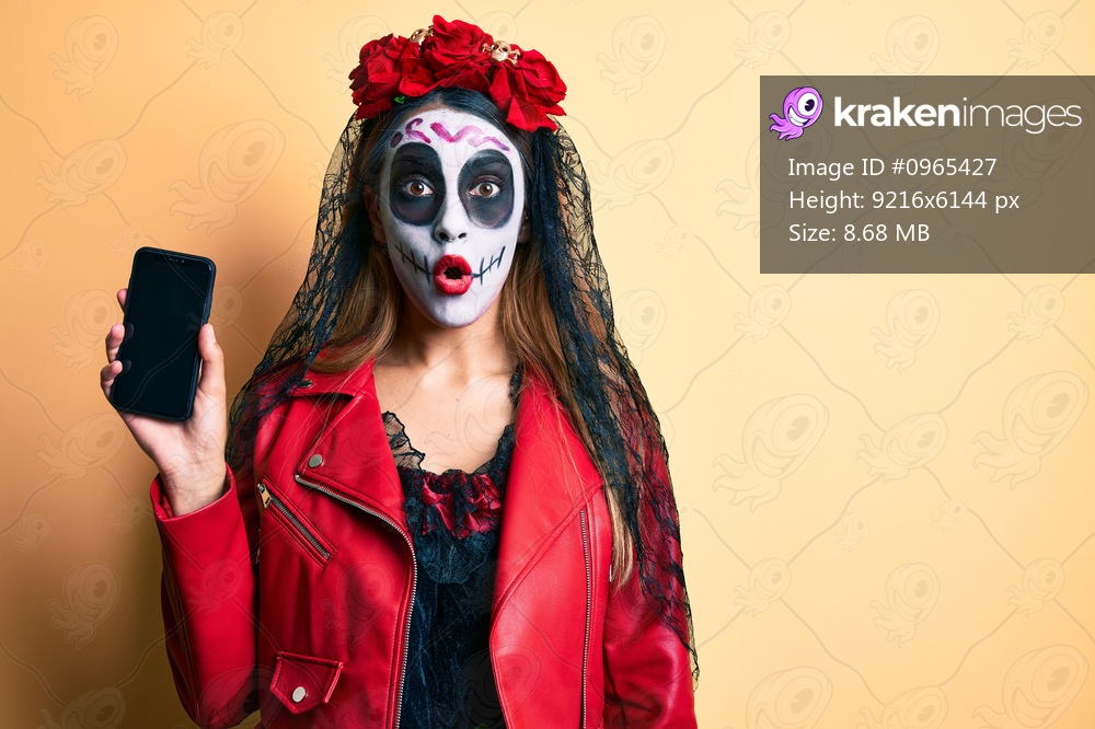Woman wearing day of the dead costume holding smartphone showing screen scared and amazed with open mouth for surprise, disbelief face 