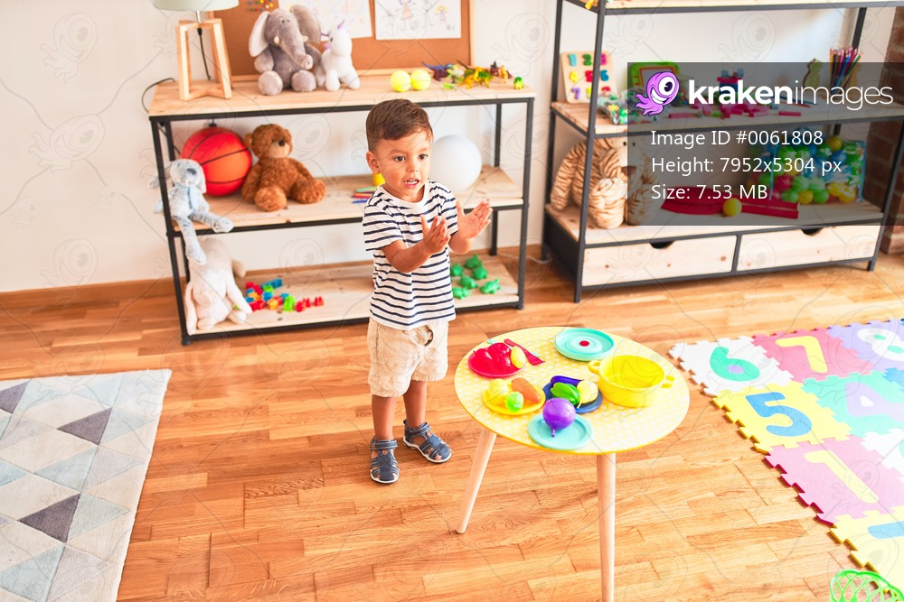 Beautiful toddler boy playing meals with plastic plates, fruits and vegetables at kindergarten