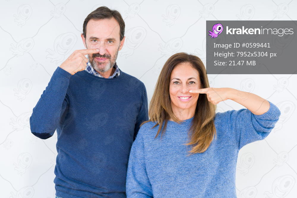 Beautiful middle age couple in love over isolated background Pointing with hand finger to face and nose, smiling cheerful