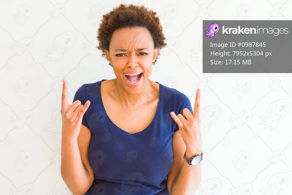 Young beautiful african american woman over white background shouting with crazy expression doing rock symbol with hands up. Music star. Heavy concept.