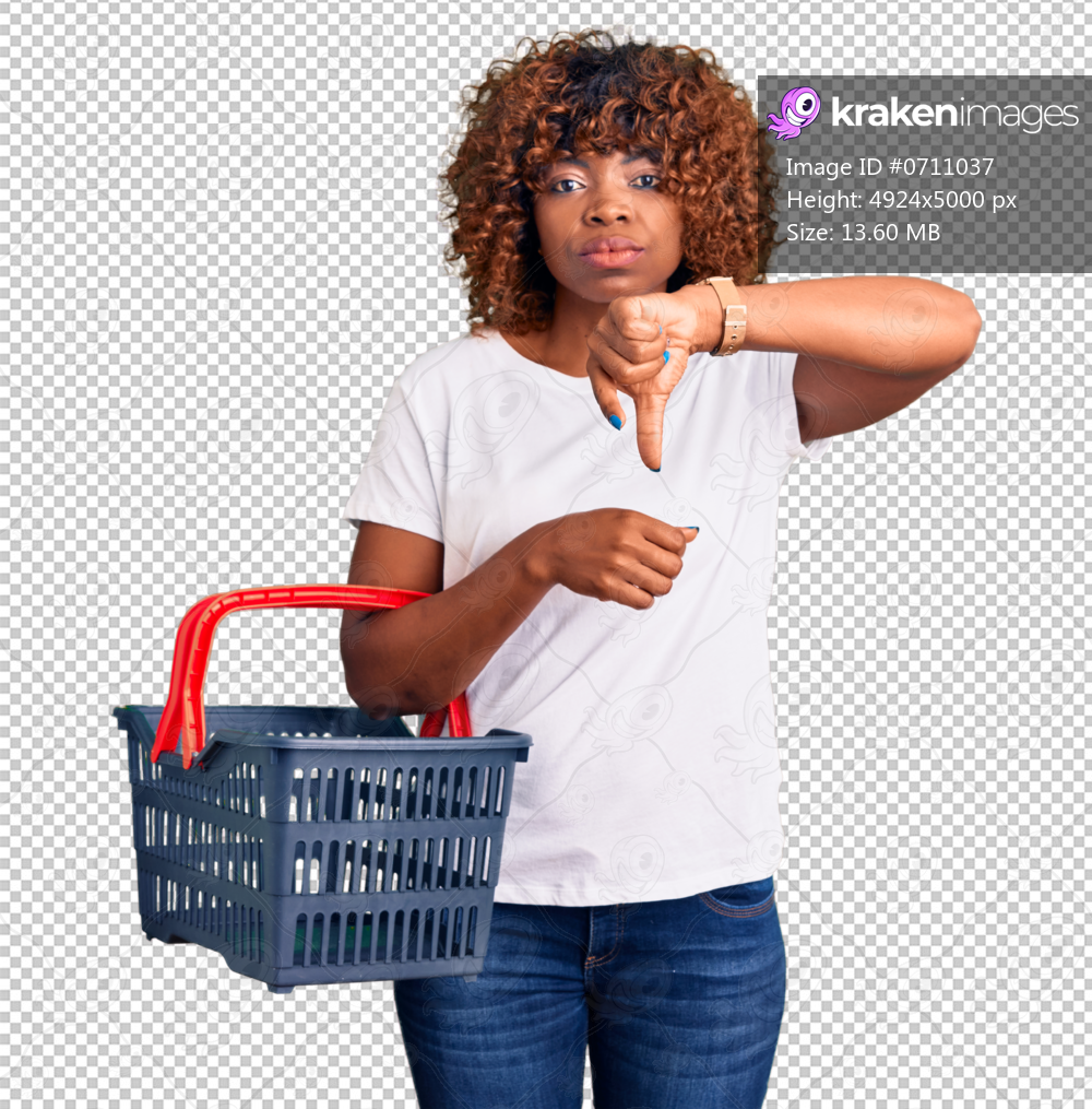 Young african american woman holding supermarket shopping basket with angry face, negative sign showing dislike with thumbs down, rejection concept