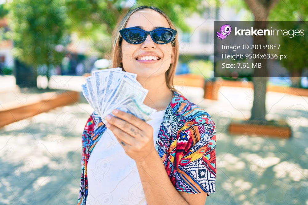 Young beautiful blonde caucasian woman smiling happy outdoors on a sunny day showing american dollars banknotes