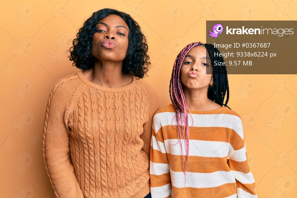 Beautiful african american mother and daughter wearing wool winter sweater looking at the camera blowing a kiss on air being lovely and sexy. love expression. 