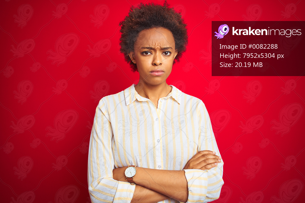 Young beautiful african american woman with afro hair over isolated red background skeptic and nervous, disapproving expression on face with crossed arms. Negative person.