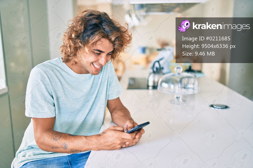 Young hispanic man smiling happy using smartphone sitting on the table at home