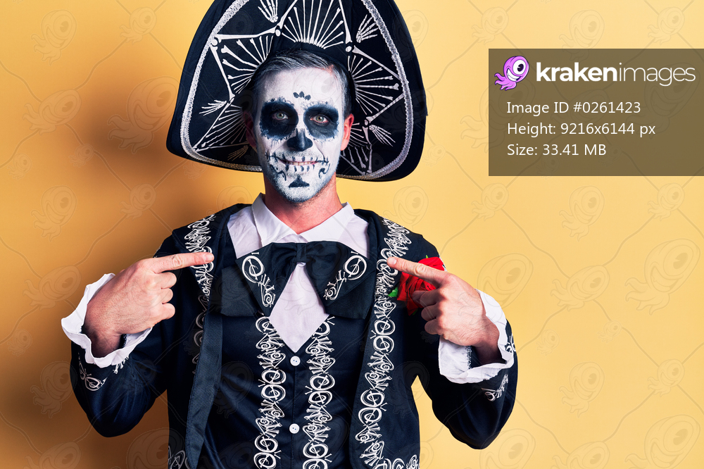 Young man wearing mexican day of the dead costume over yellow looking confident with smile on face, pointing oneself with fingers proud and happy. 