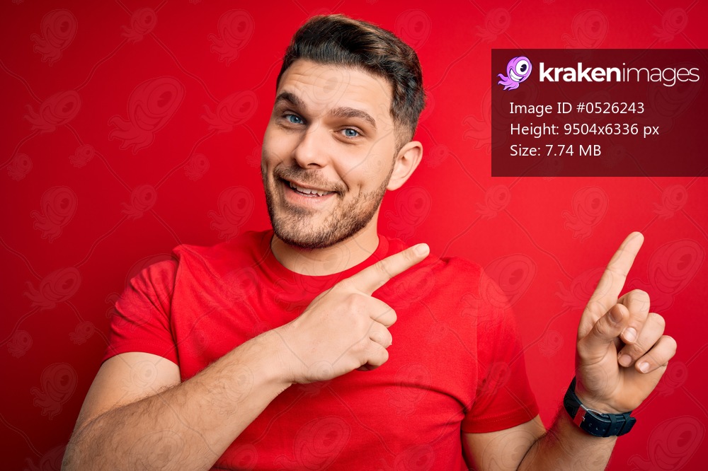 Young man with blue eyes wearing casual t-shirt over red isolated background smiling and looking at the camera pointing with two hands and fingers to the side.