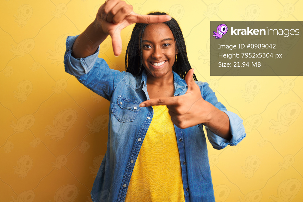 Young african american woman wearing denim shirt standing over isolated yellow background smiling making frame with hands and fingers with happy face. Creativity and photography concept.