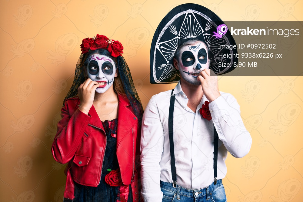 Couple wearing day of the dead costume over yellow looking stressed and nervous with hands on mouth biting nails. anxiety problem. 