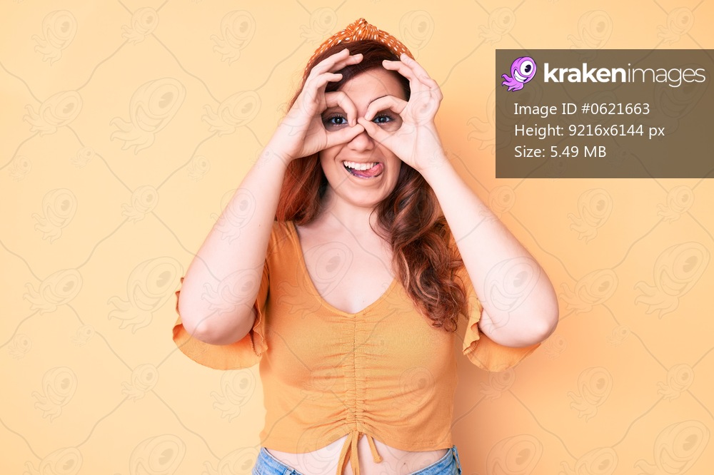 Young beautiful woman wearing casual clothes doing ok gesture like binoculars sticking tongue out, eyes looking through fingers. crazy expression. 