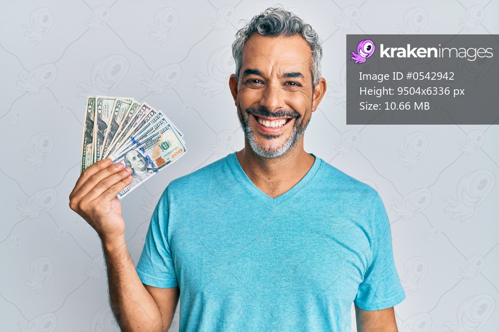Middle age grey-haired man holding dollars looking positive and happy standing and smiling with a confident smile showing teeth 