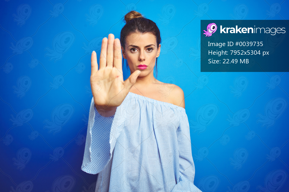 Young beautiful woman wearing bun hairstyle over blue isolated background doing stop sing with palm of the hand. Warning expression with negative and serious gesture on the face.