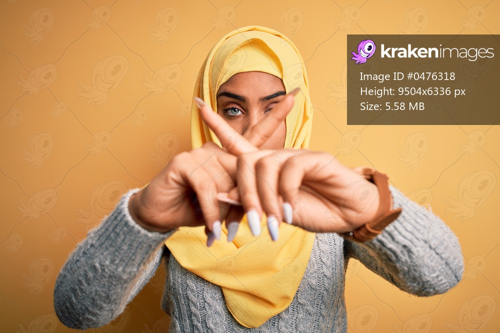 Young beautiful african american girl wearing muslim hijab over isolated yellow background Rejection expression crossing fingers doing negative sign