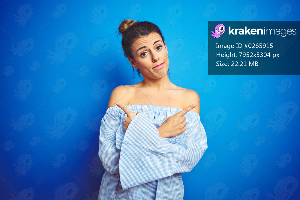 Young beautiful woman wearing bun hairstyle over blue isolated background Pointing to both sides with fingers, different direction disagree