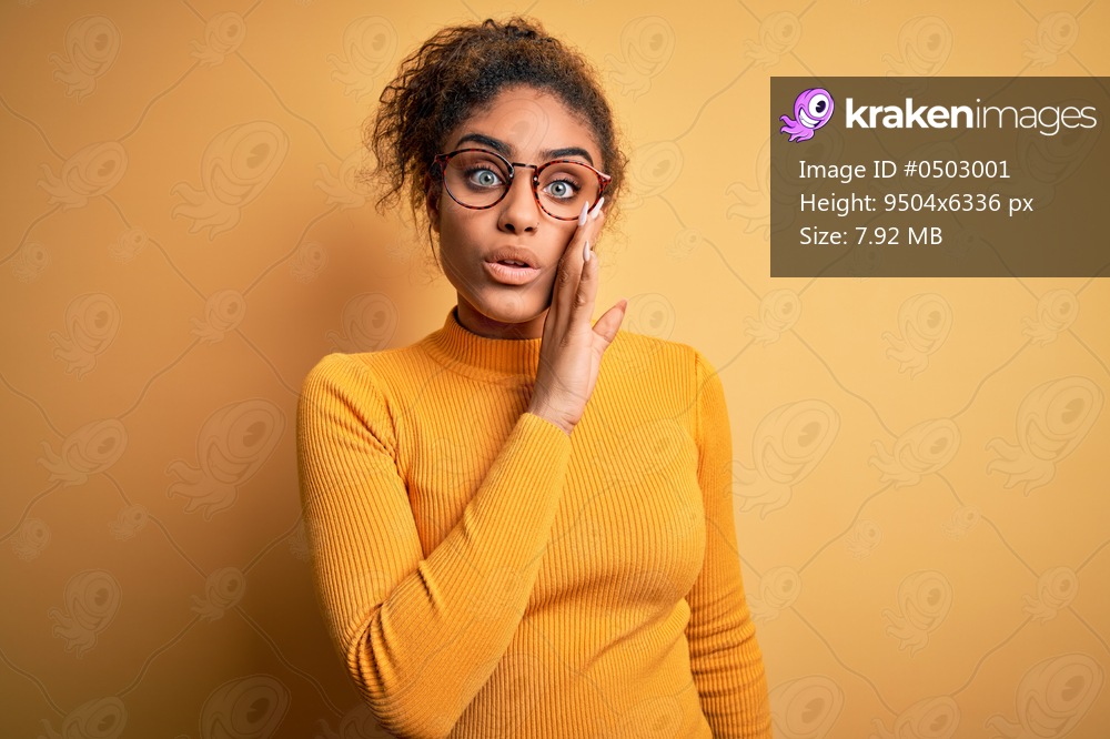 Young beautiful african american girl wearing sweater and glasses over yellow background hand on mouth telling secret rumor, whispering malicious talk conversation