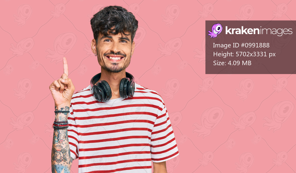 Young hispanic man listening to music using headphones showing and pointing up with finger number one while smiling confident and happy. 