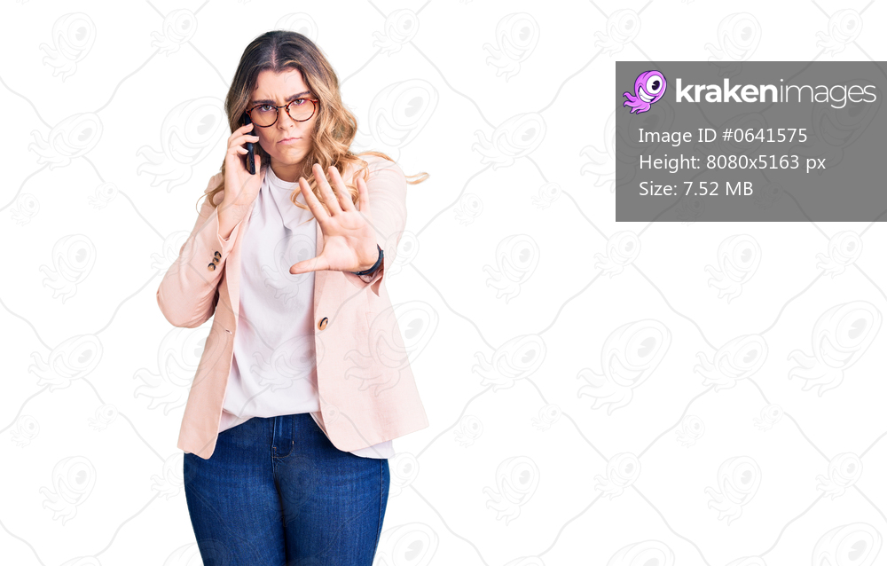 Young caucasian woman having conversation talking on the smartphone with open hand doing stop sign with serious and confident expression, defense gesture 