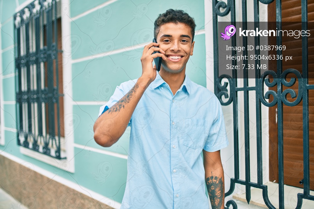 Young latin man smiling happy using smartphone walking at the city.