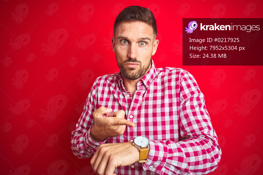 Young handsome man over red isolated background In hurry pointing to watch time, impatience, upset and angry for deadline delay