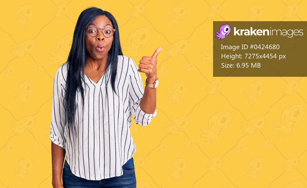 Young african american woman wearing casual clothes and glasses surprised pointing with hand finger to the side, open mouth amazed expression. 