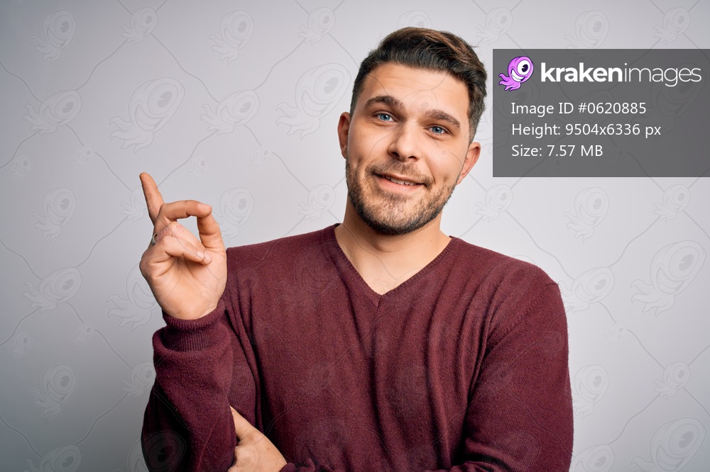 Young man with blue eyes wearing casual sweater standing over isolated background with a big smile on face, pointing with hand and finger to the side looking at the camera.