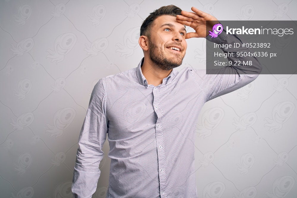 Young business man with blue eyes standing over isolated background very happy and smiling looking far away with hand over head. Searching concept.