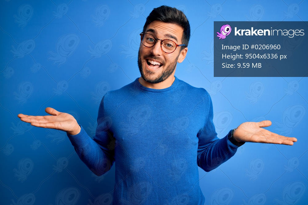 Young handsome man with beard wearing casual sweater and glasses over blue background smiling showing both hands open palms, presenting and advertising comparison and balance