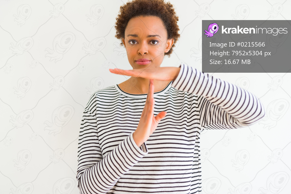 Young beautiful african american woman wearing stripes sweater over white background Doing time out gesture with hands, frustrated and serious face