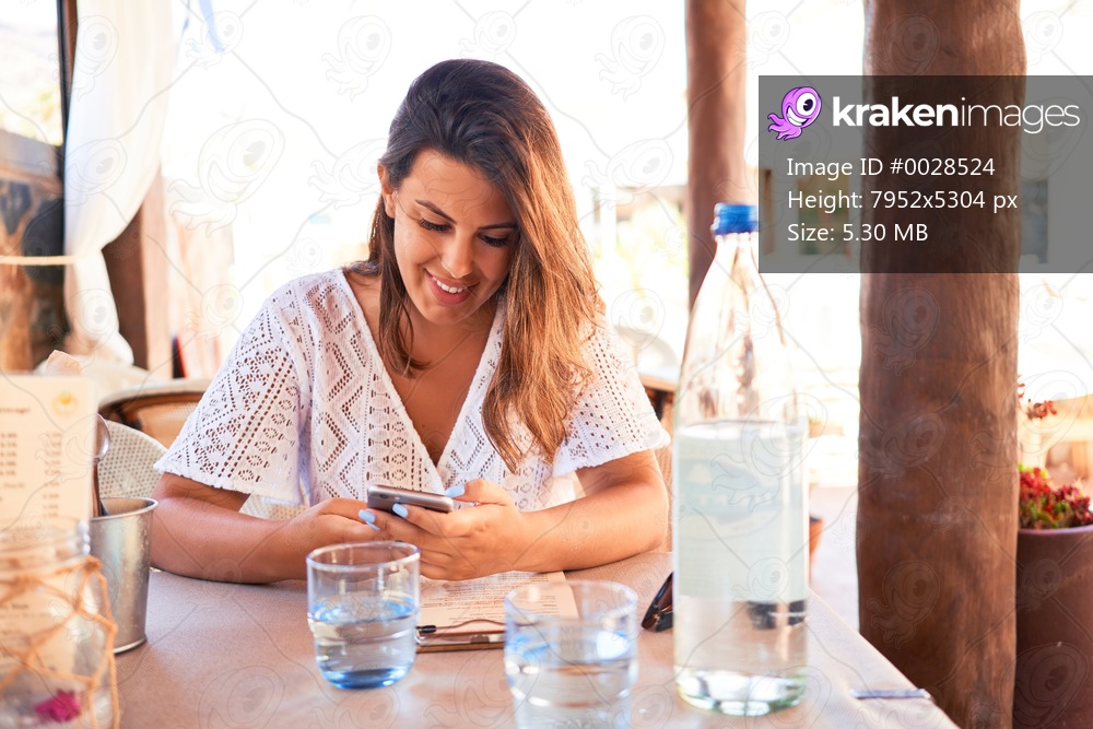Young beautiful woman sitting at restaurant enjoying summer vacation using smartphone
