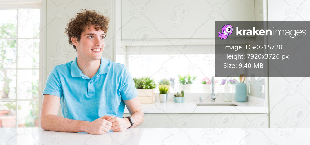 Wide shot of young handsome man at home looking away to side with smile on face, natural expression. Laughing confident.