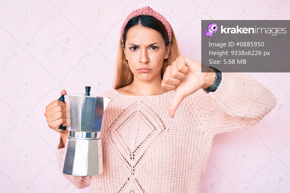 Young brunette woman holding italian coffee maker with angry face, negative sign showing dislike with thumbs down, rejection concept 