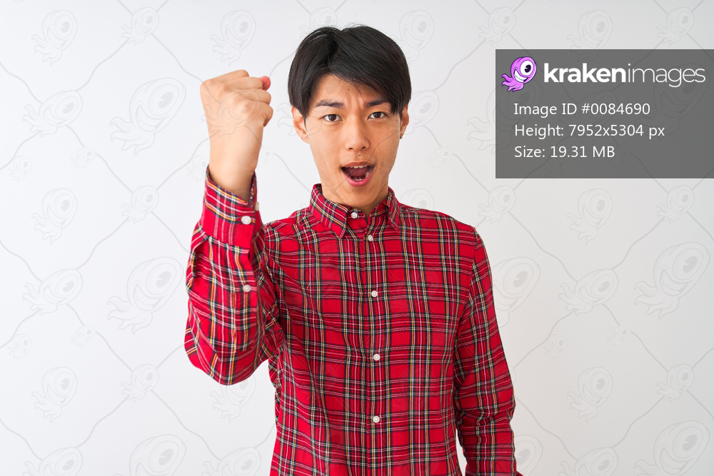 Young chinese man wearing casual red shirt standing over isolated white background angry and mad raising fist frustrated and furious while shouting with anger. Rage and aggressive concept.
