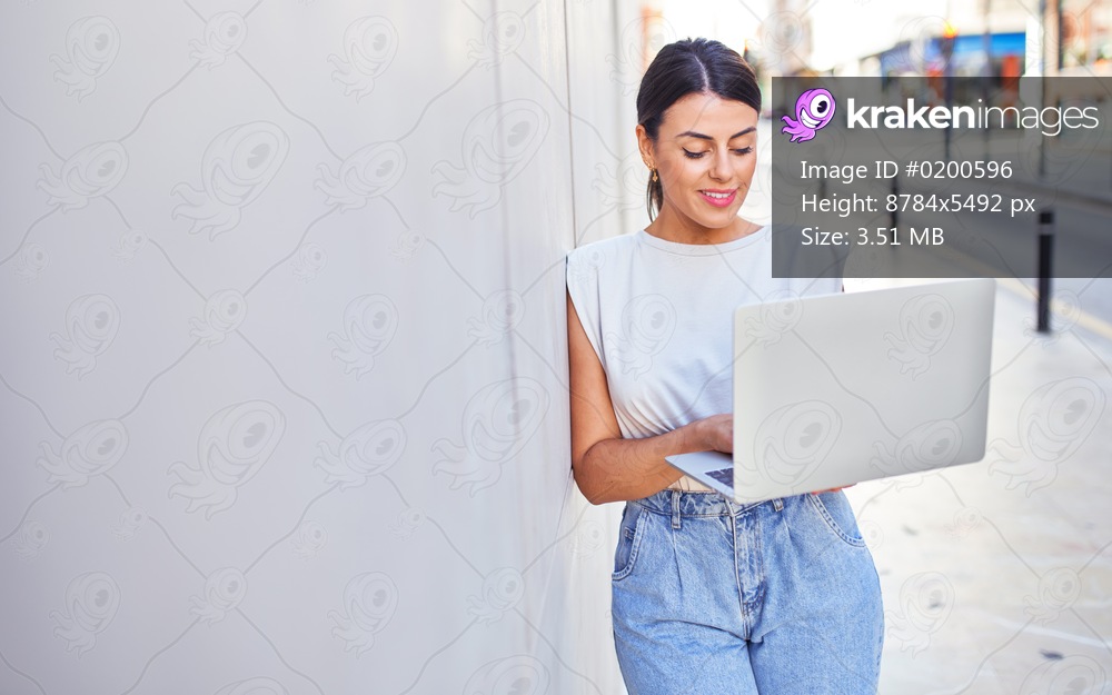 Beautiful young woman wearing fashionable clothes walking down the street and working using computer laptop