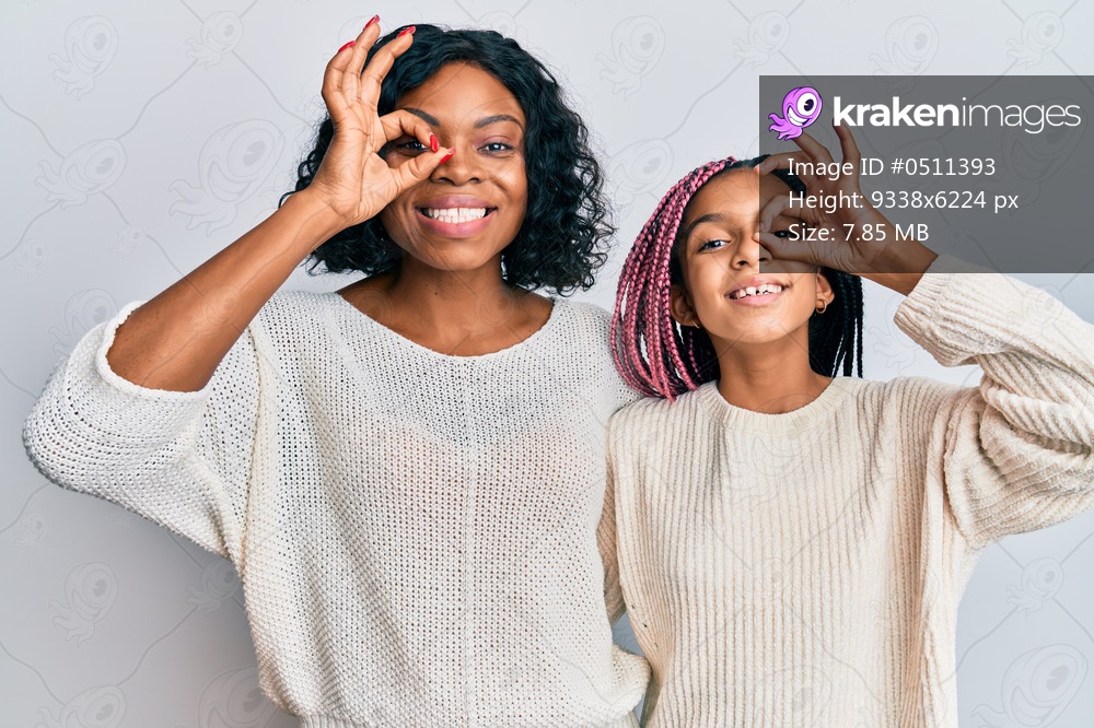 Beautiful african american mother and daughter wearing casual clothes and hugging doing ok gesture with hand smiling, eye looking through fingers with happy face. 