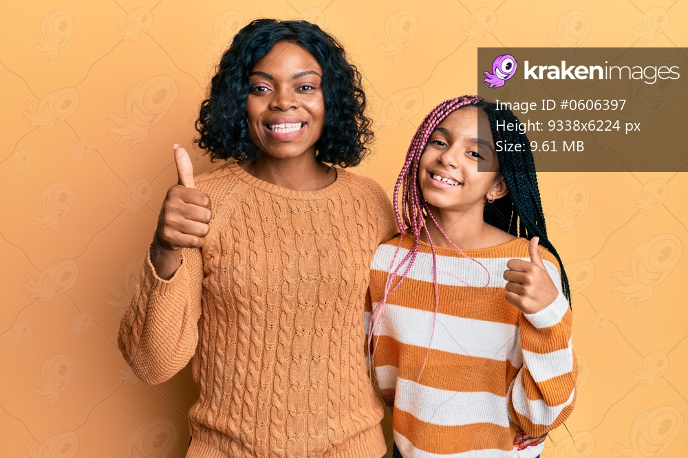 Beautiful african american mother and daughter wearing wool winter sweater success sign doing positive gesture with hand, thumbs up smiling and happy. cheerful expression and winner gesture. 
