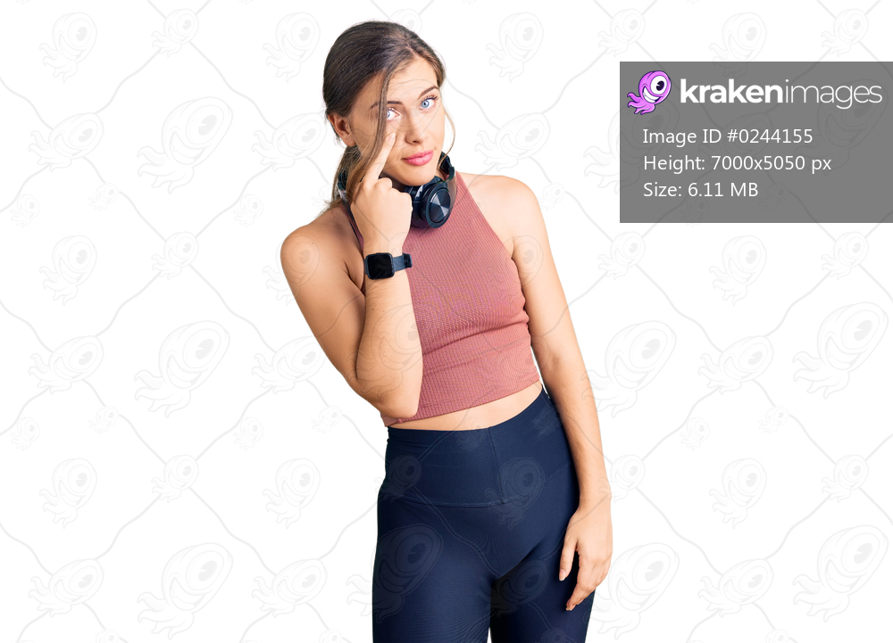 Beautiful caucasian young woman wearing gym clothes and using headphones pointing to the eye watching you gesture, suspicious expression 