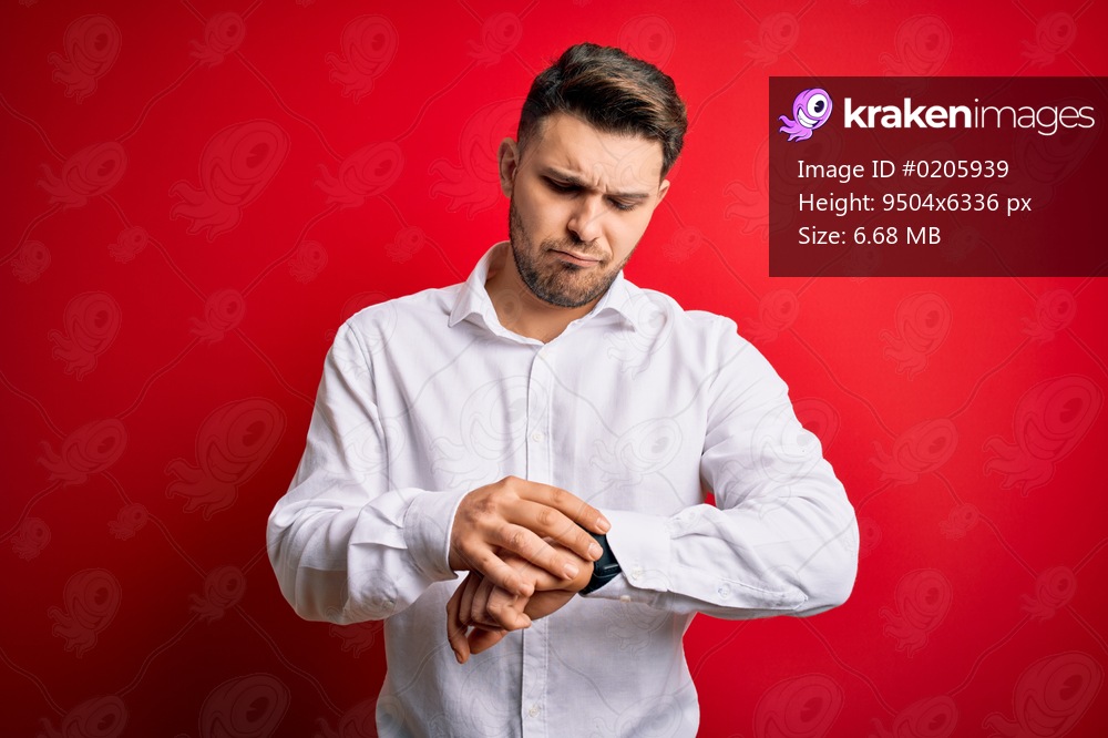 Young business man with blue eyes wearing elegant shirt standing over red isolated background Checking the time on wrist watch, relaxed and confident