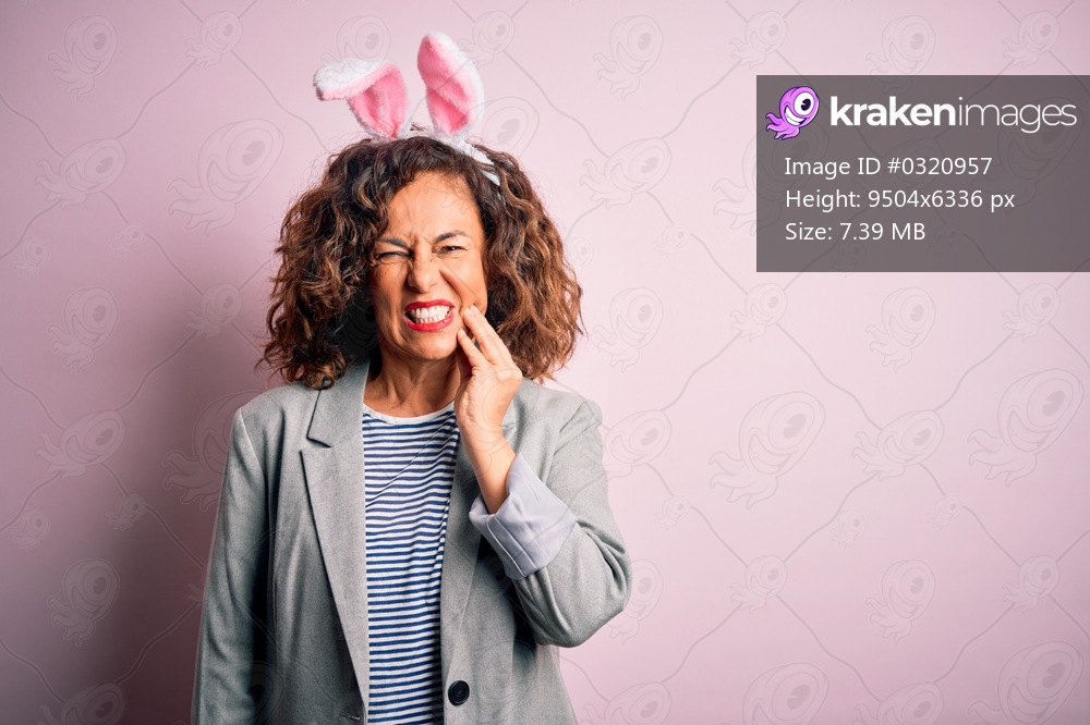 Middle age beautiful woman wearing bunny ears standing over isolated pink background touching mouth with hand with painful expression because of toothache or dental illness on teeth. Dentist