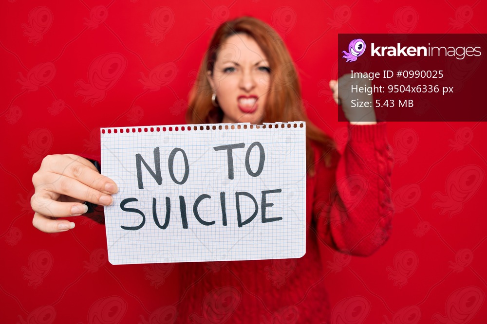 Beautiful redhead woman holding banner showing no to suicide message over red background annoyed and frustrated shouting with anger, crazy and yelling with raised hand, anger concept