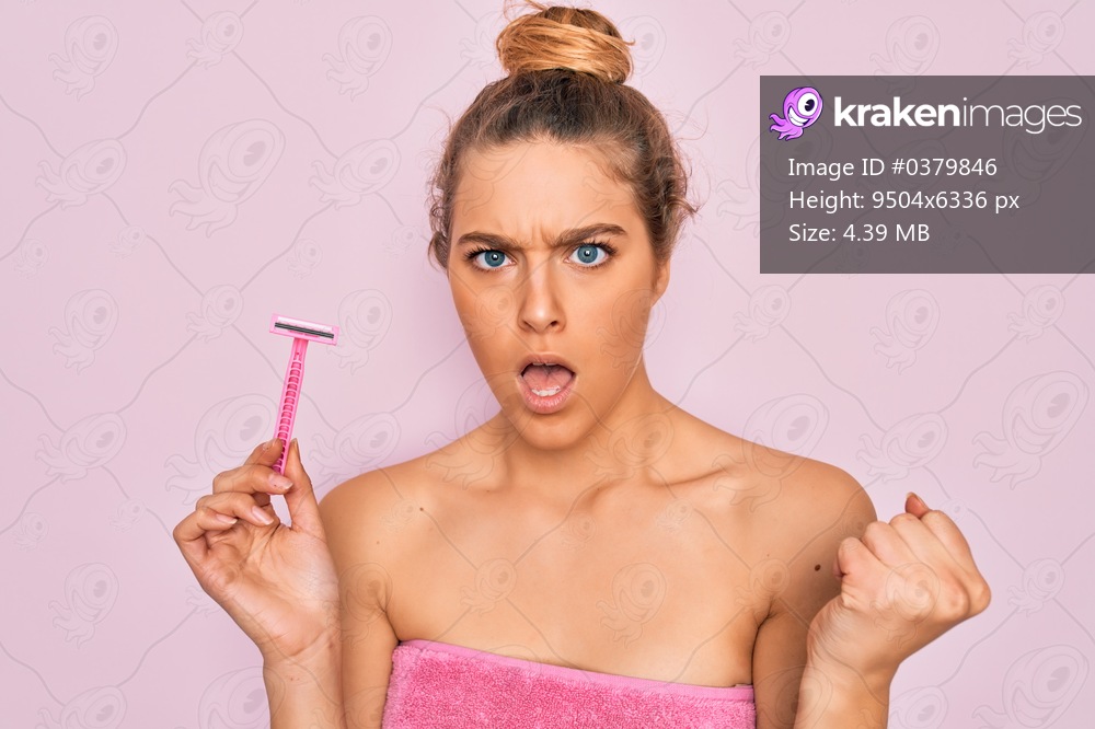 Beautiful woman with blue eyes wearing towel shower after bath holding depilation razon annoyed and frustrated shouting with anger, crazy and yelling with raised hand, anger concept