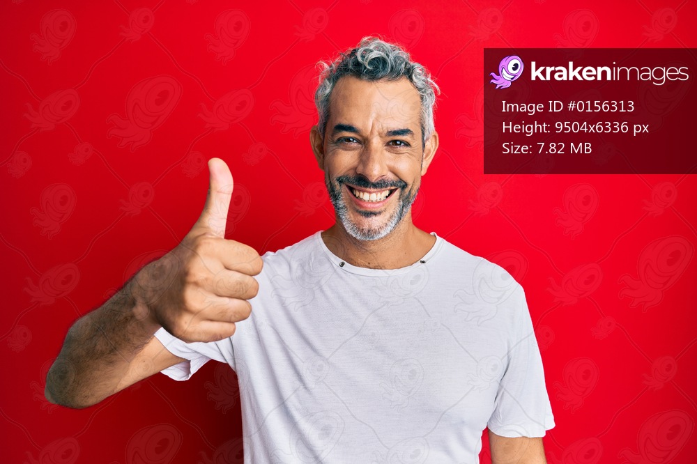 Middle age grey-haired man wearing casual white tshirt smiling happy and positive, thumb up doing excellent and approval sign 