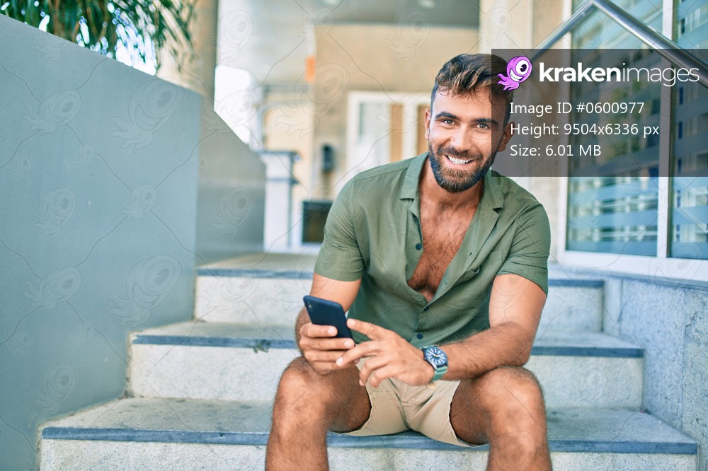 Young hispanic man smiling happy using smartphone sitting on stairs