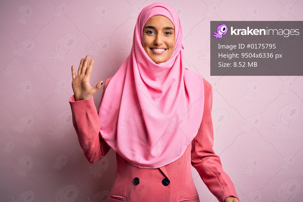 Young beautiful brunette businesswoman wearing pink muslim hijab and business jacket showing and pointing up with fingers number five while smiling confident and happy.