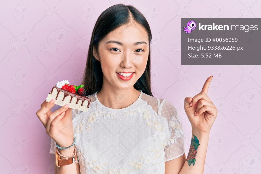 Young chinese woman eating a tasty cake smiling happy pointing with hand and finger to the side 